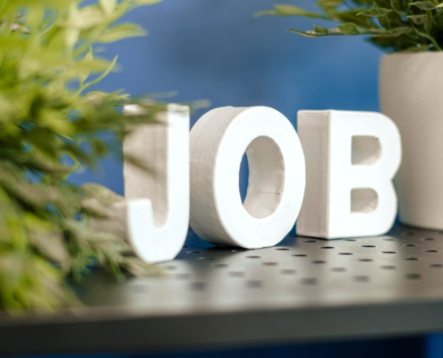 Das Wort Job steht in weißen Buchstaben vor blauem Hintergrund und Grünpflanzen