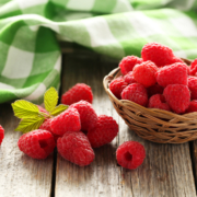 Ein Körbchen mit Himbeeren auf einem Holztisch mit einem grün-weiß-karierten Geschirrtuch
