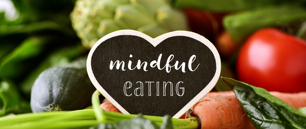 Die Worte mindful eating stehen auf einem Kreidetafel-Herz, welches auf Gemüse liegt
