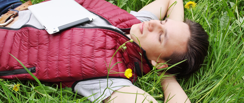 Junger Mann liegt entspannt mit geschlossenen Augen im Gras